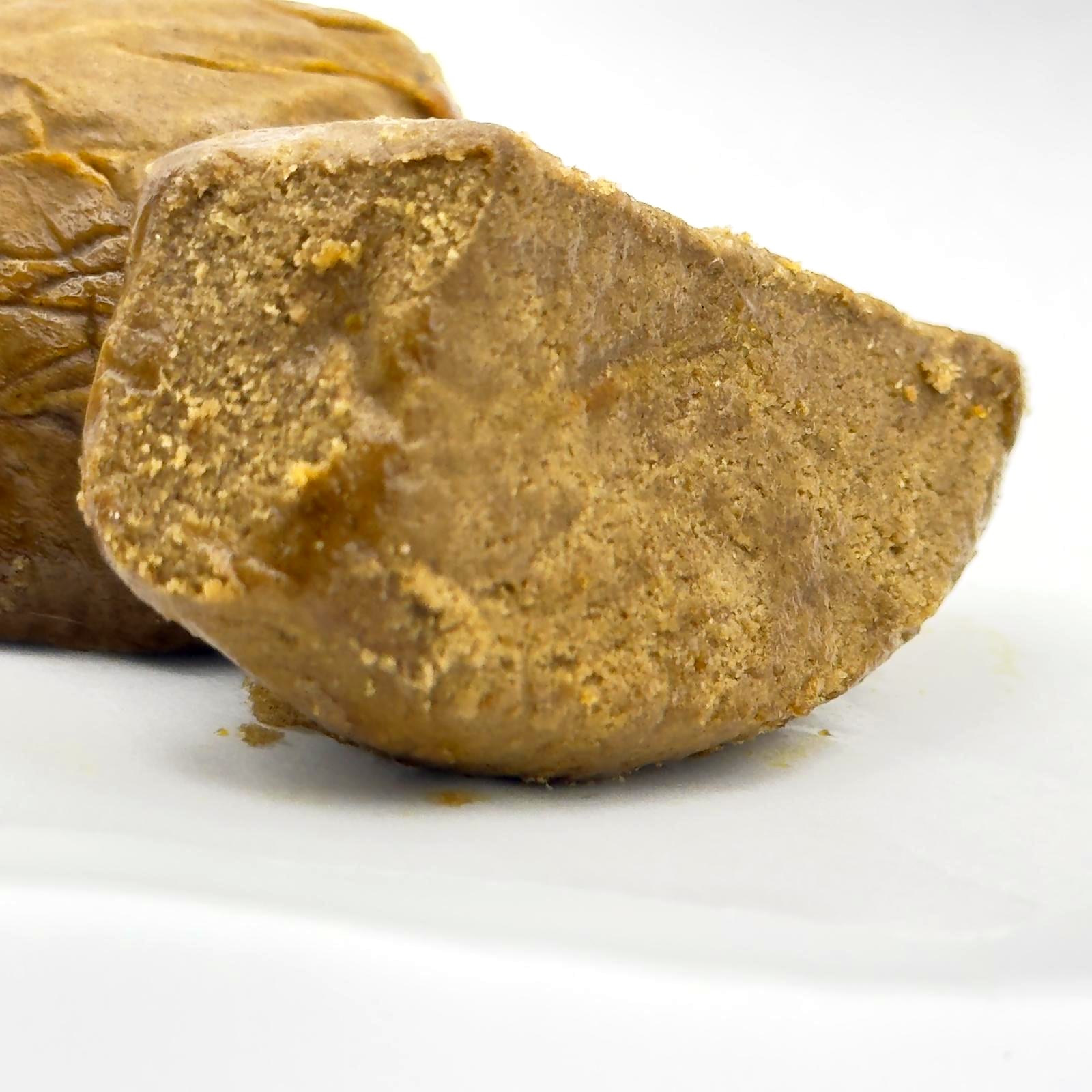 The broken face of the piece in close-up: a dense, sandy texture, paler at the core, in front of the whole block